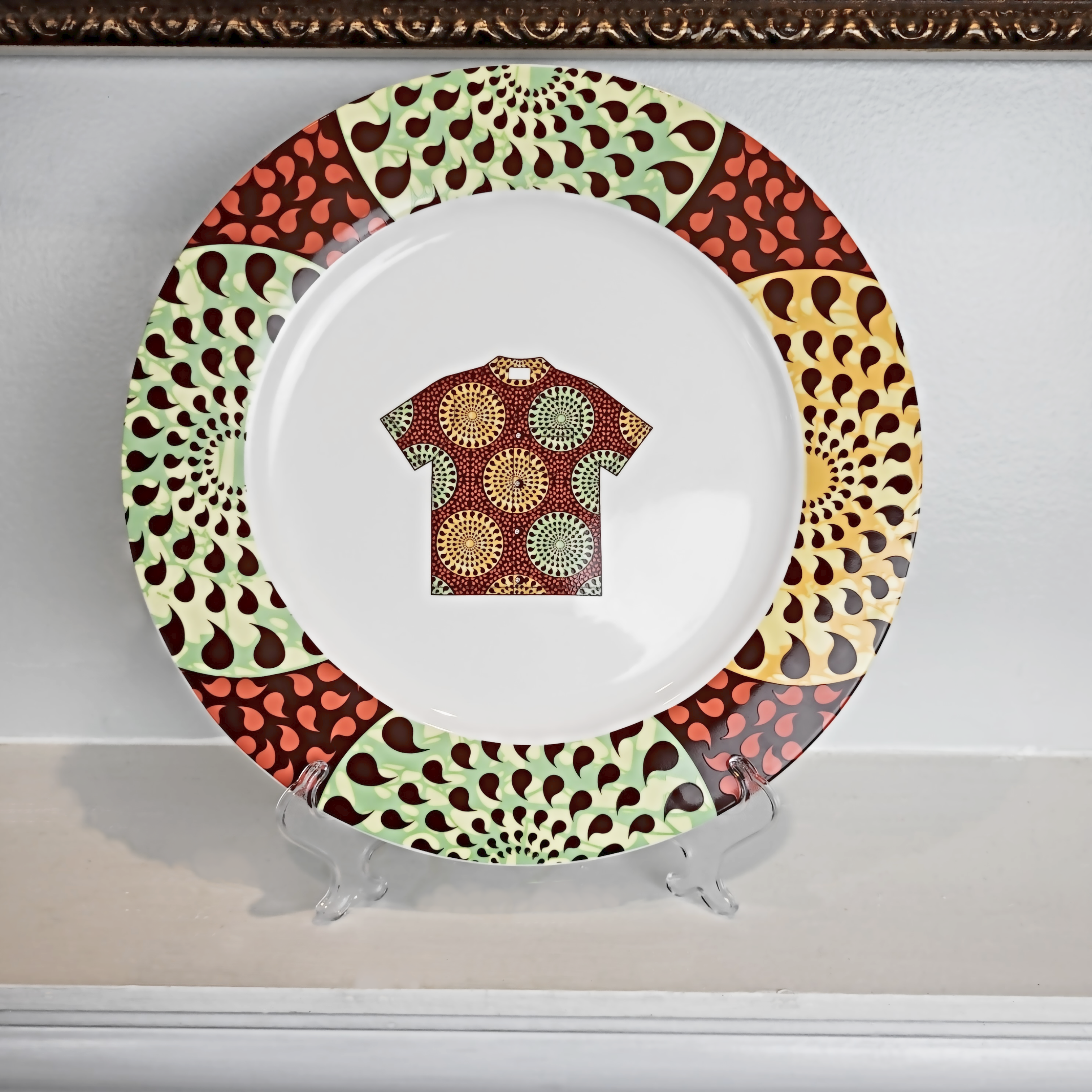 Colorful and beautilful African art dinner plate with African art in paisley pattern around its rim. In the center of the plate is an African shirt with the same paisley artwork on it.