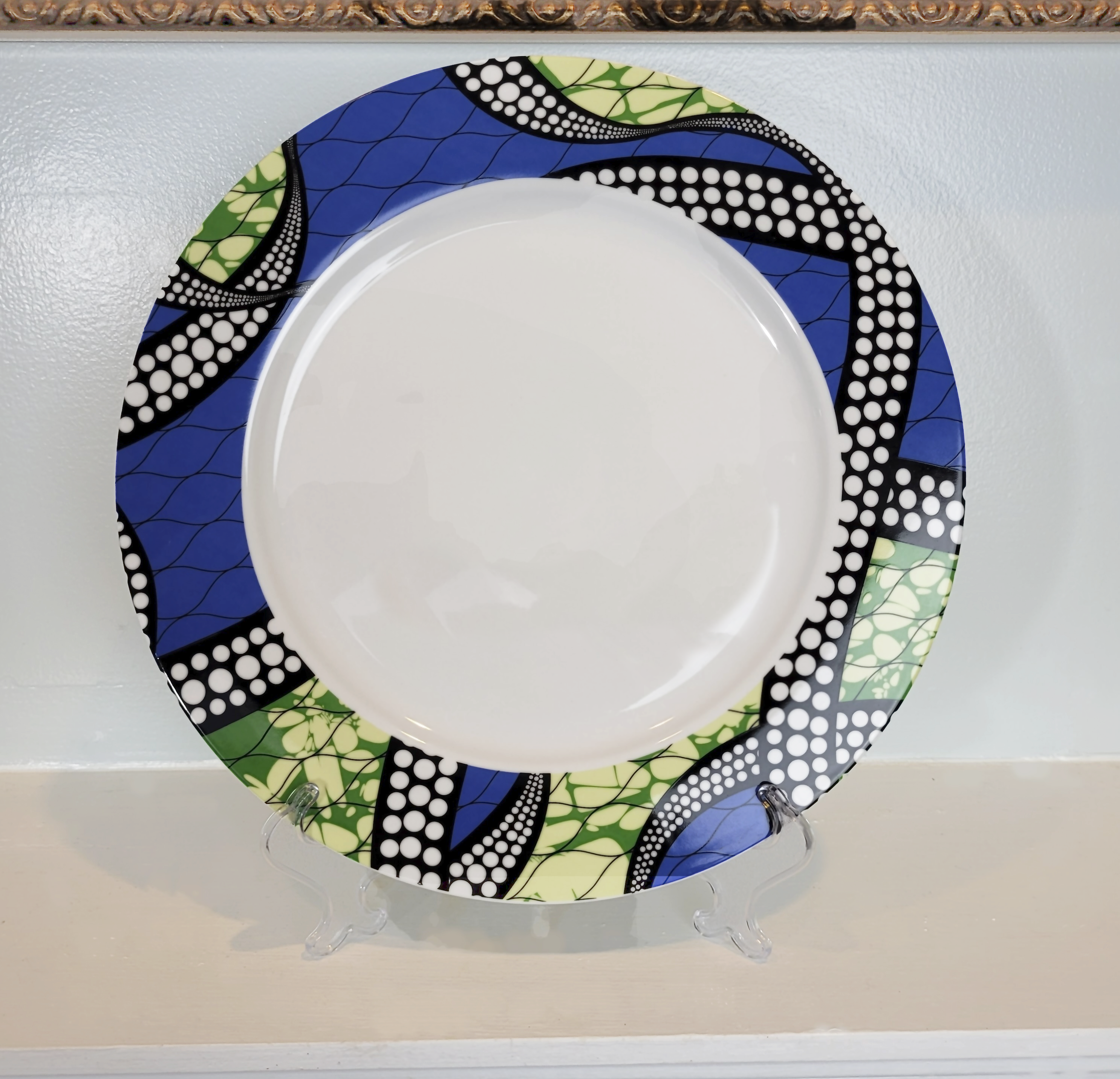 This is a ceramic plate with abstract African patterns around the rim of the plate. In the art you can see a flat black rope with white polka dots like pearls, looping randomly around the plate.